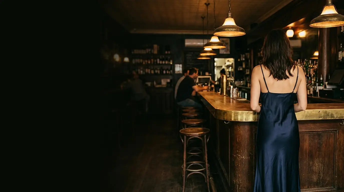 Woman in blue dress standing at wooden bar in dimly lit pub
