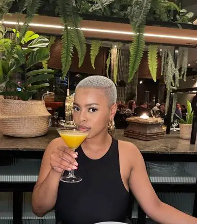 Woman with short hair holding cocktail in upscale restaurant with lush plant decor