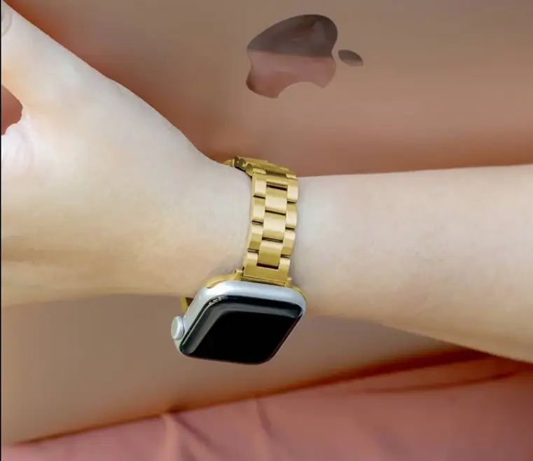Smartwatch with gold metal band on wrist holding laptop with visible logo