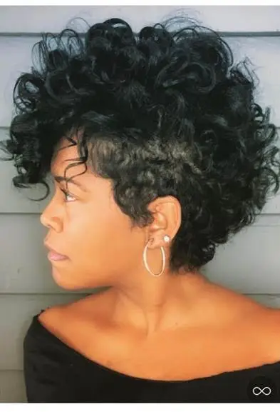 Woman with short curly hair wearing hoop earrings against gray wall