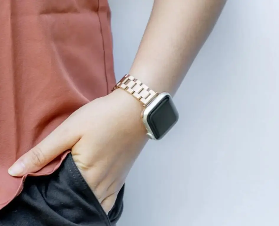Person wearing rose gold smartwatch and placing hand in pocket against white background