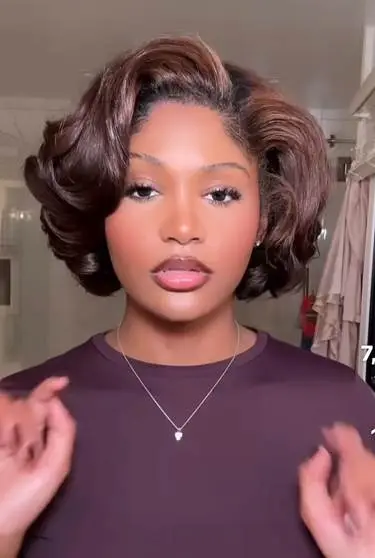Woman with stylish short wavy hair wearing a purple top and necklace indoors
