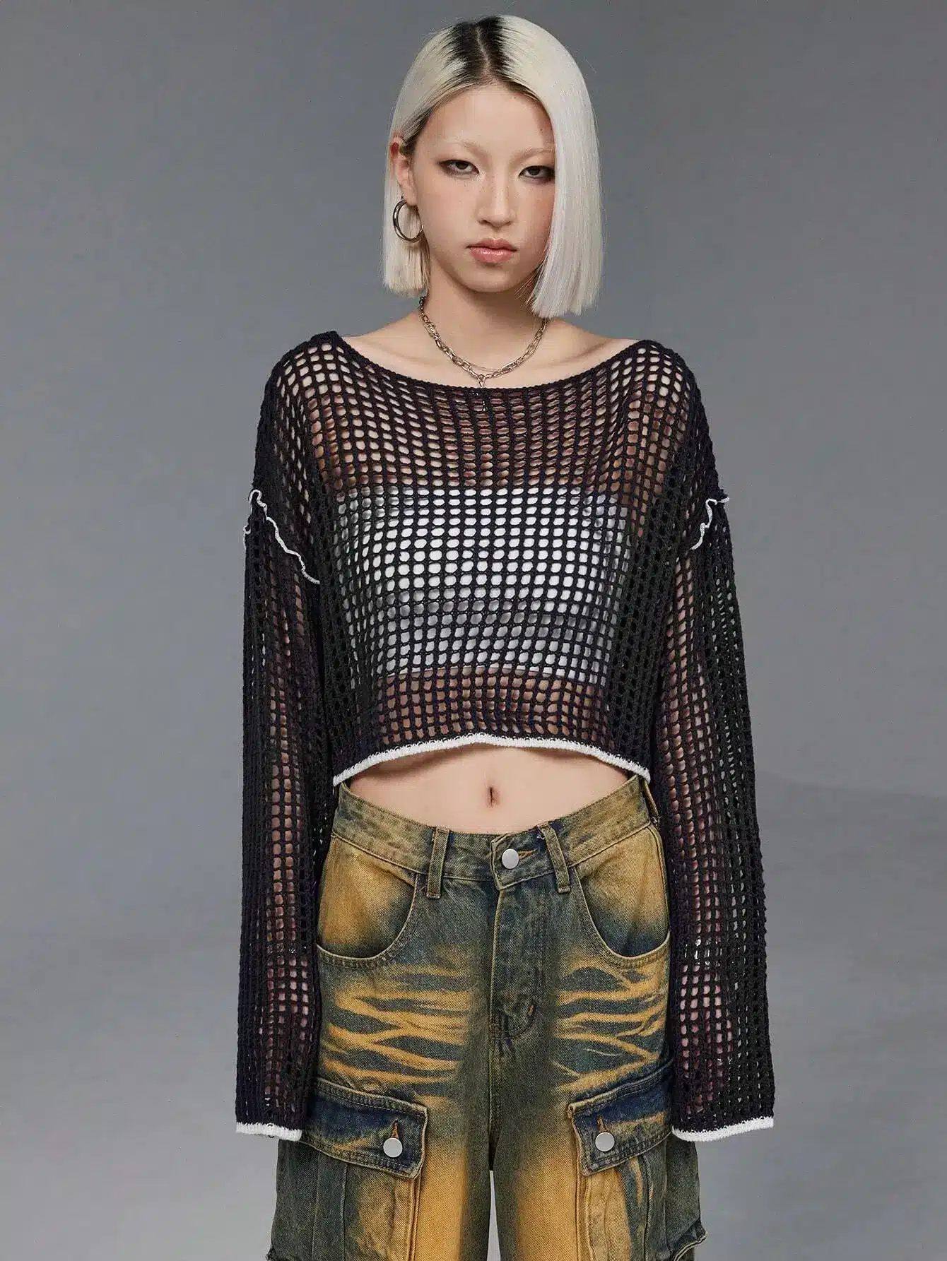 Blonde person wearing black mesh top and yellow distressed jeans in studio setting