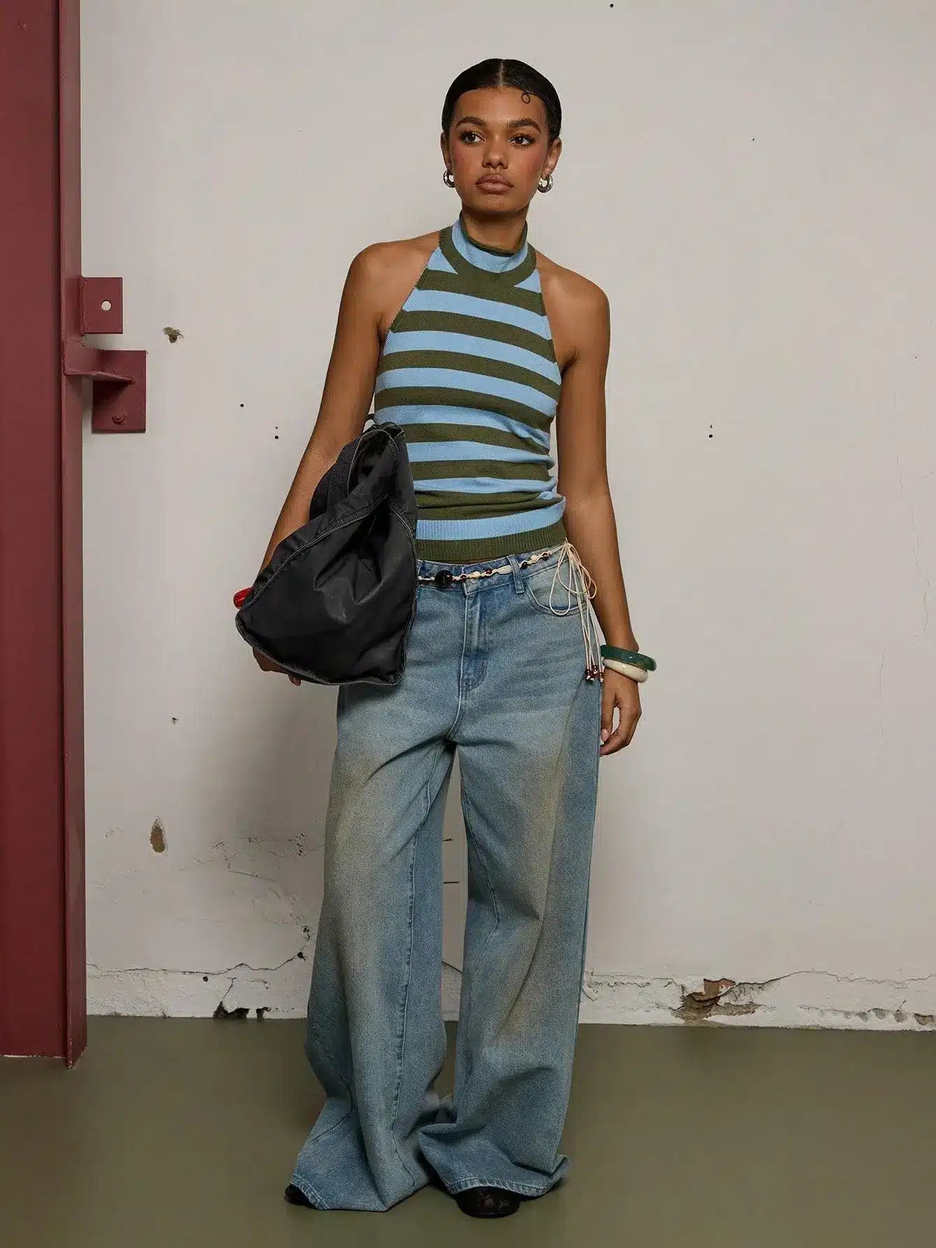 Person wearing striped halter top and wide-leg jeans holding a black bag indoors