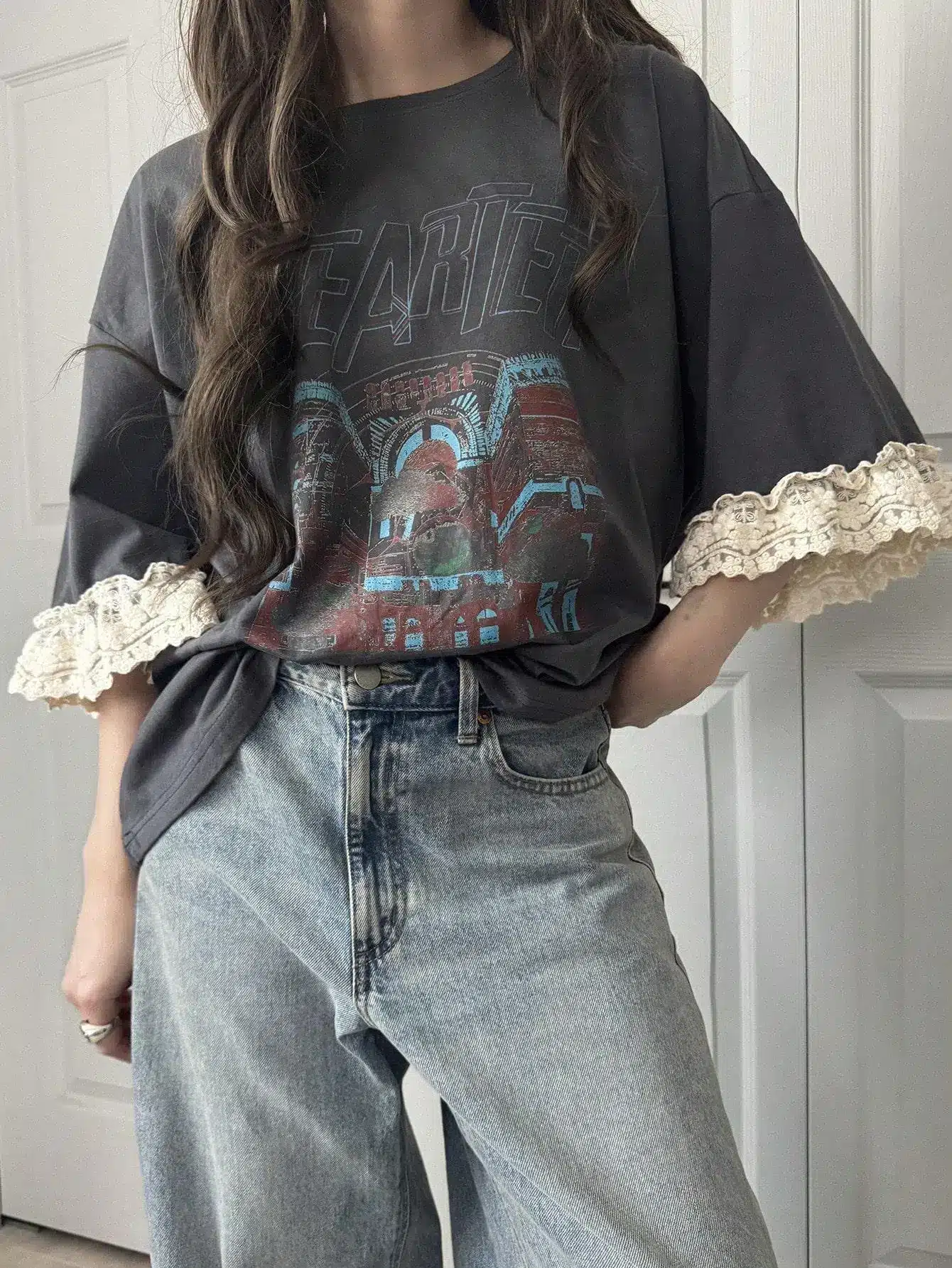 Woman wearing oversized graphic t-shirt with lace sleeves and light blue jeans indoors