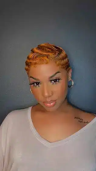 Woman with styled orange hair and hoop earrings against a dark background