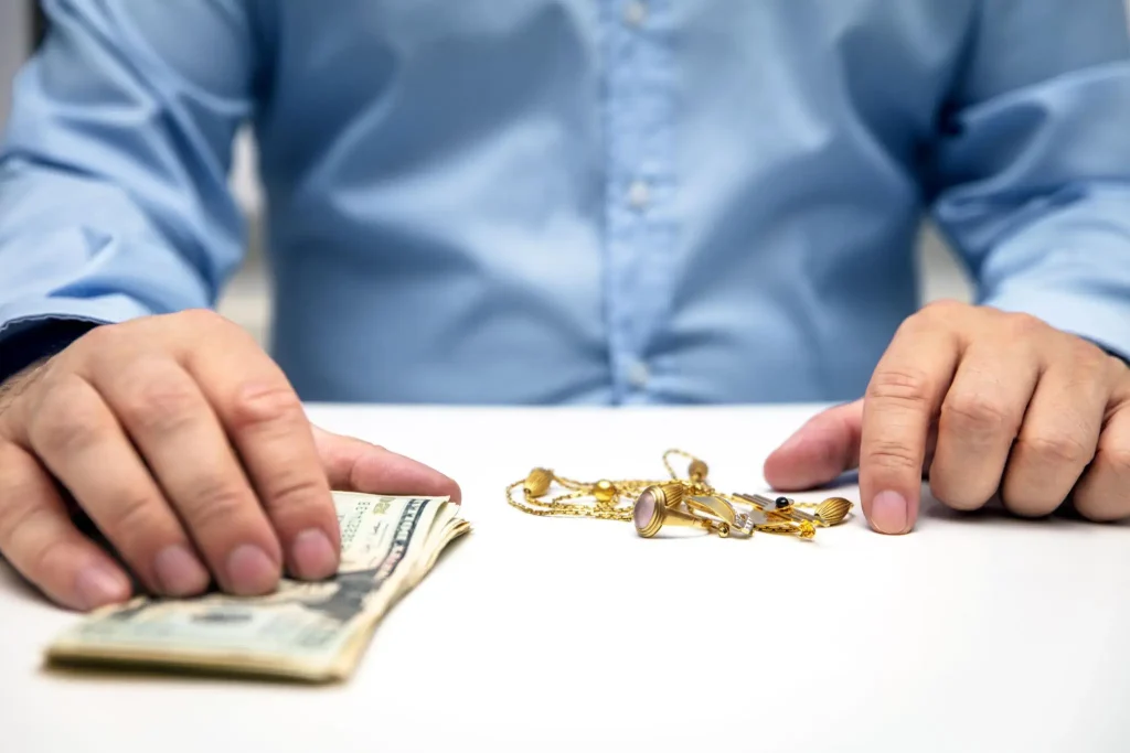 Man in blue shirt placing cash and jewelry on white table surface
