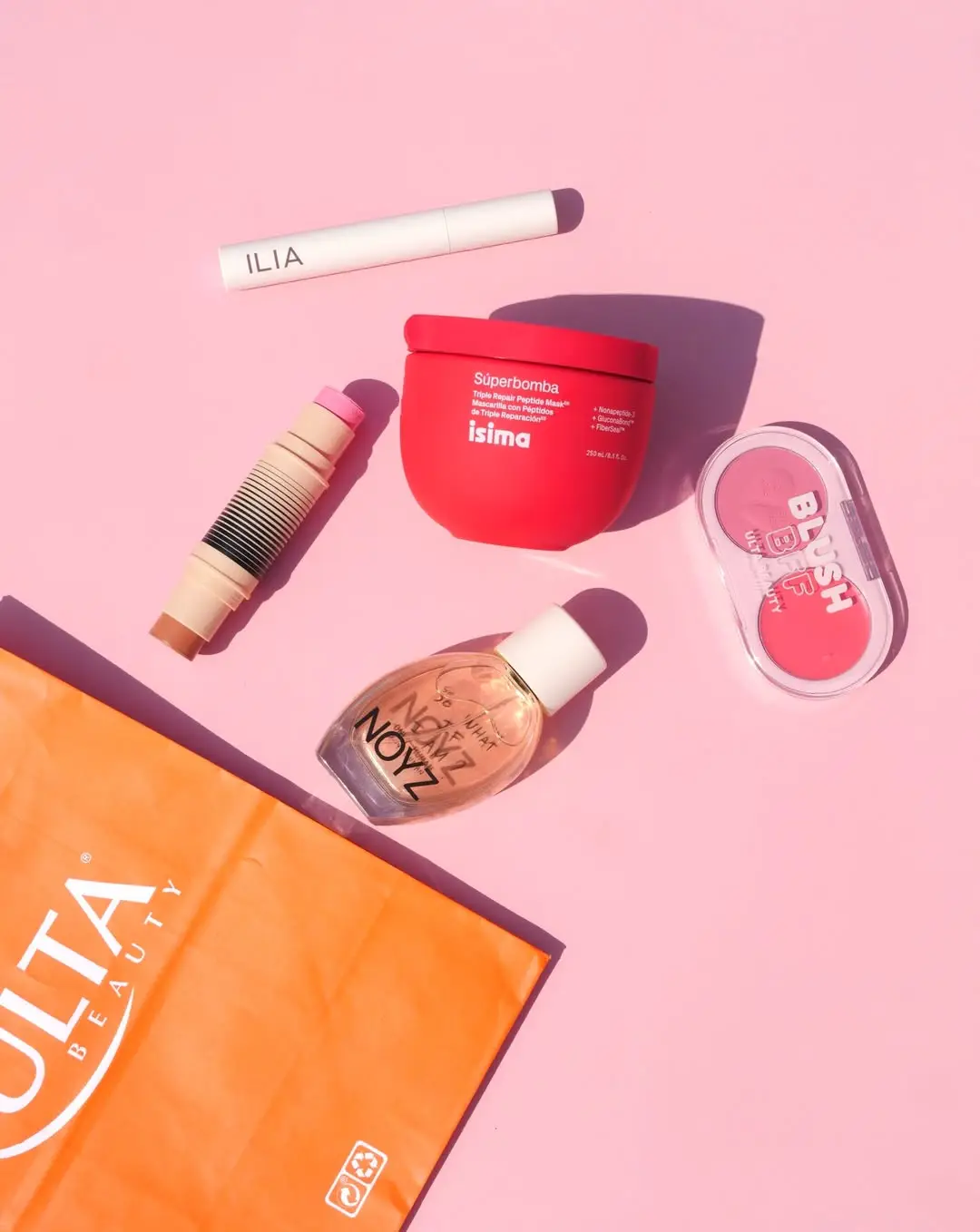 Assorted beauty products on pink background with orange shopping bag at the bottom left