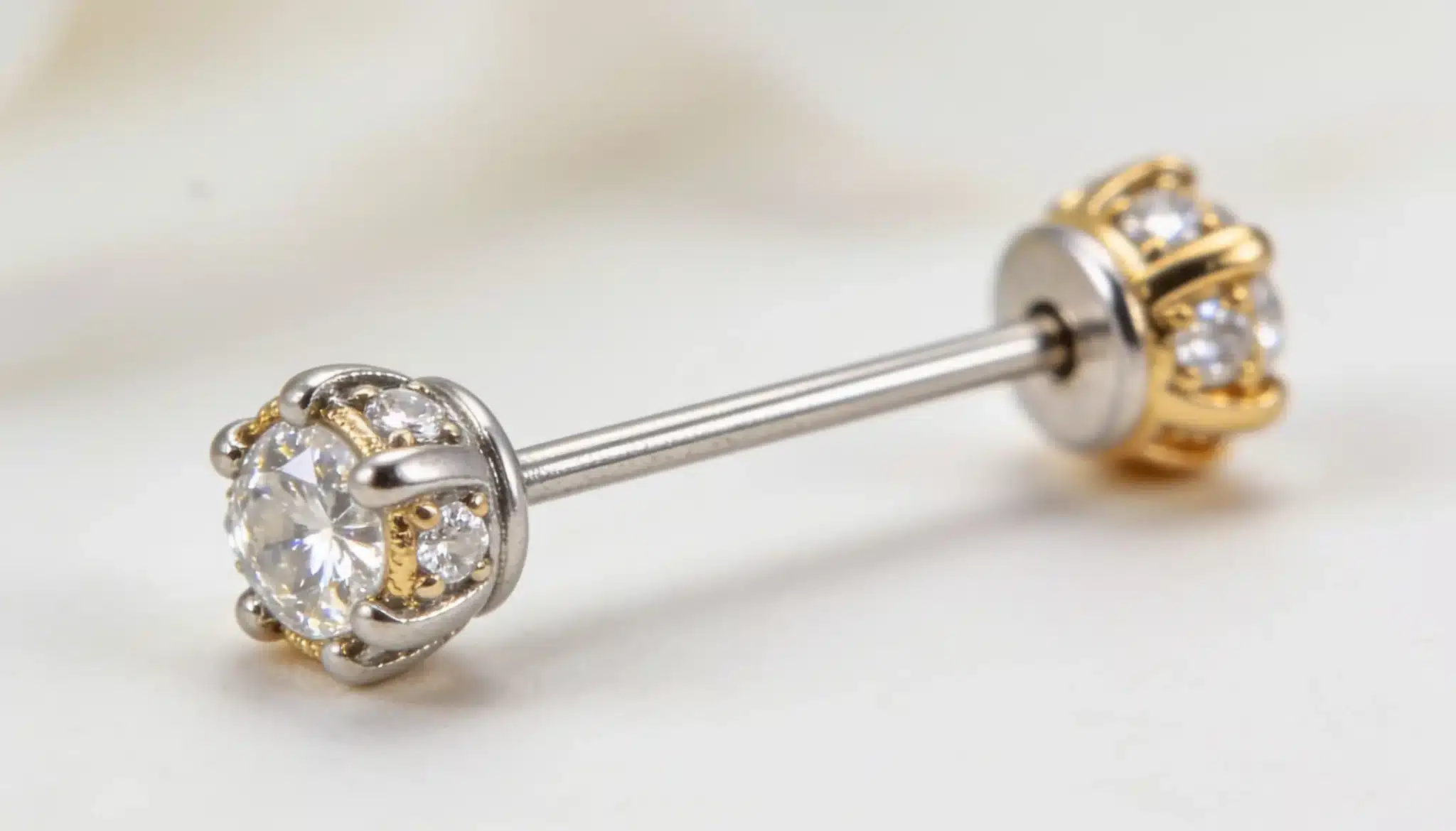 Close-up of a single barbell earring with clear stones in silver and gold setting.