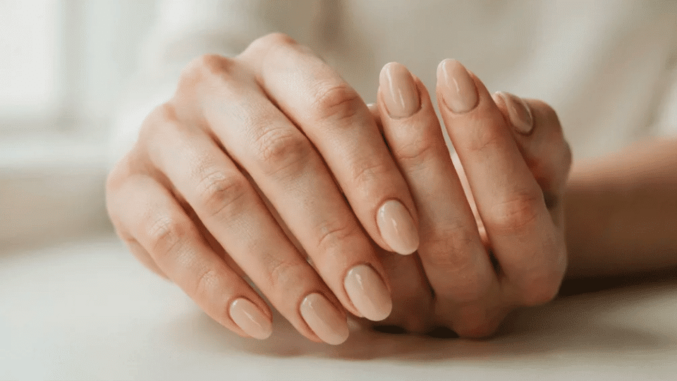 Hands with almond-shaped beige nails in matte finish, minimalist chic look for work or casual events.