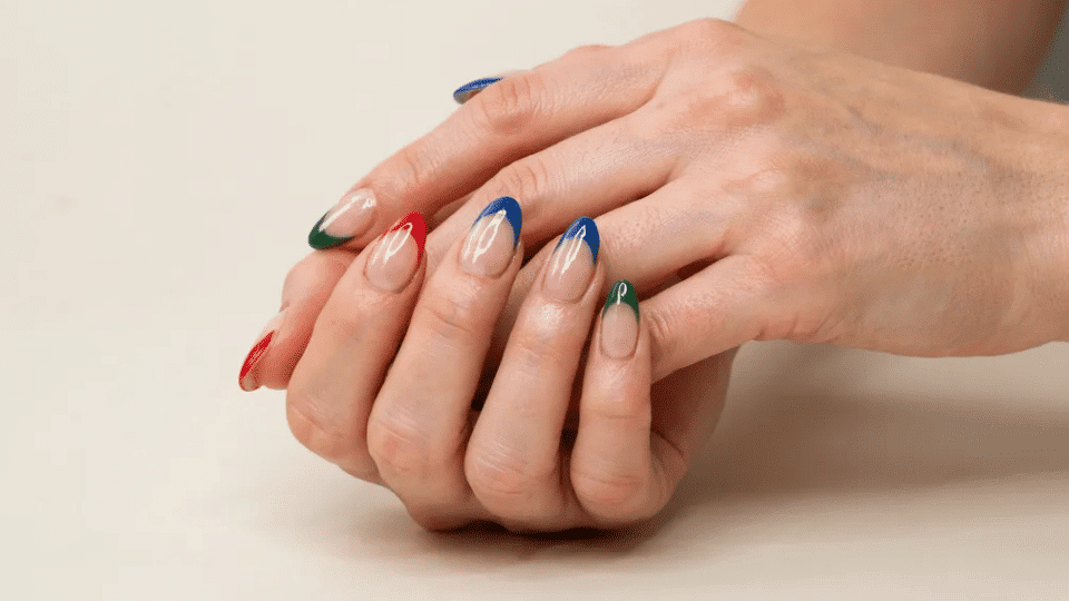 Almond-shaped nails with bold red, blue, and green tips, glossy finish, dramatic polished look.
