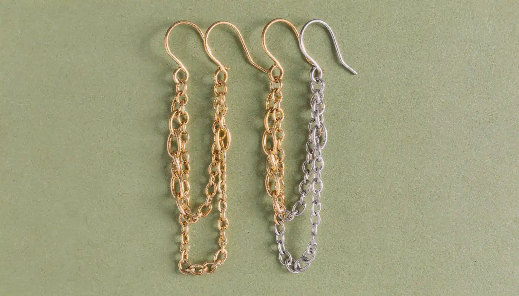 Four chain-style earrings in gold and silver laid out on green background.