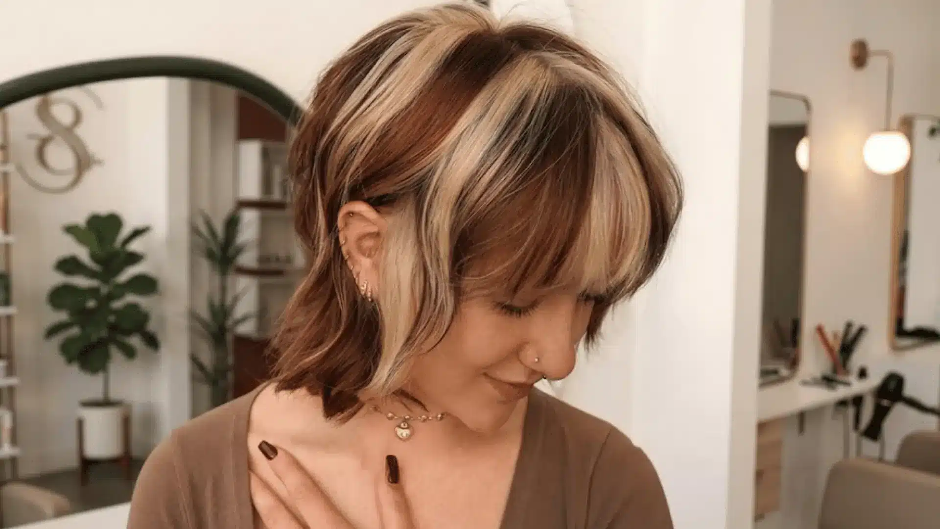 Woman with a brown and blonde chunky highlighted bob haircut inside a salon.