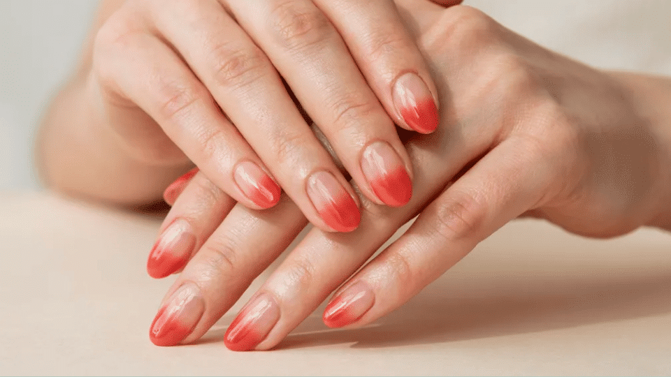 Hands showing almond nails with coral ombré from peachy nude to deep coral, glossy sun-kissed summer look.