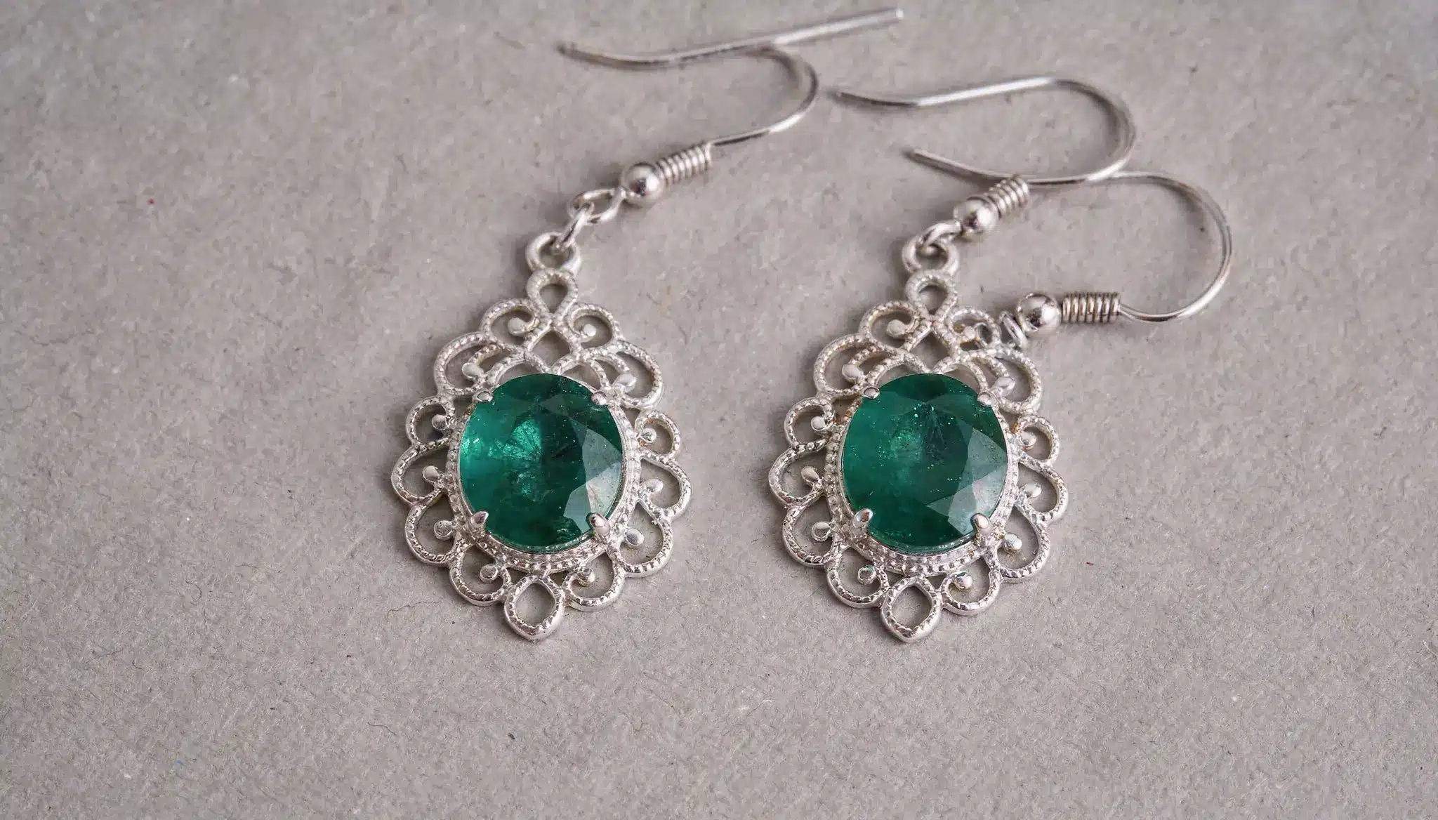 Silver dangle earrings with oval green gemstones and ornate filigree frame.