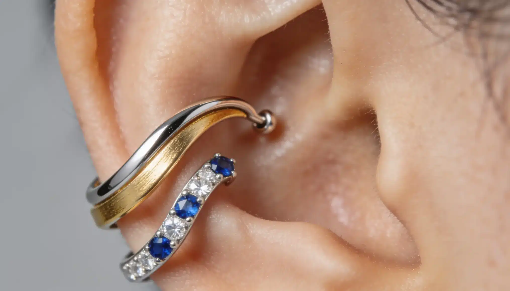 Silver and gold ear climber style earrings with small blue stones on ear.