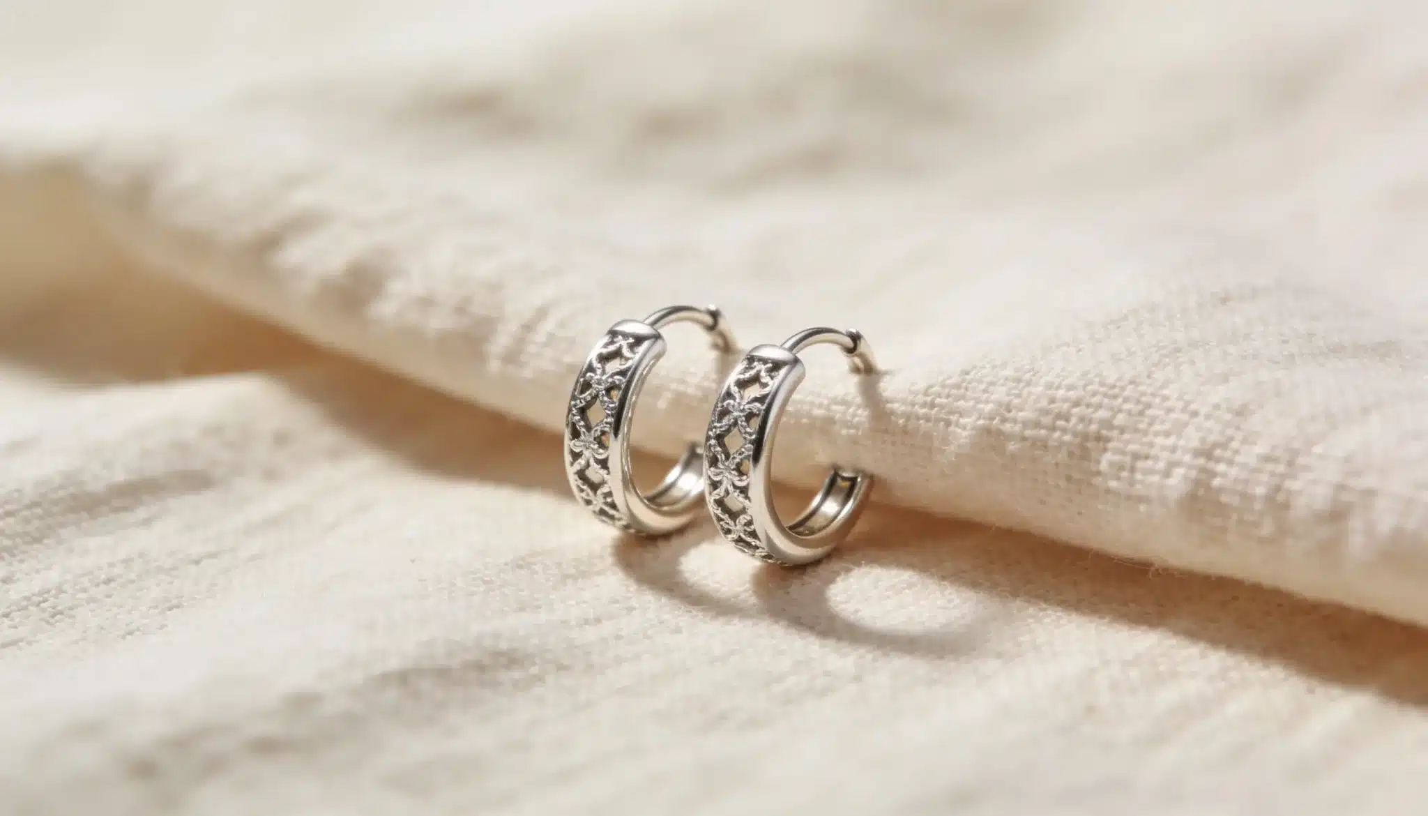 Silver huggie earrings with delicate floral cut-out design.