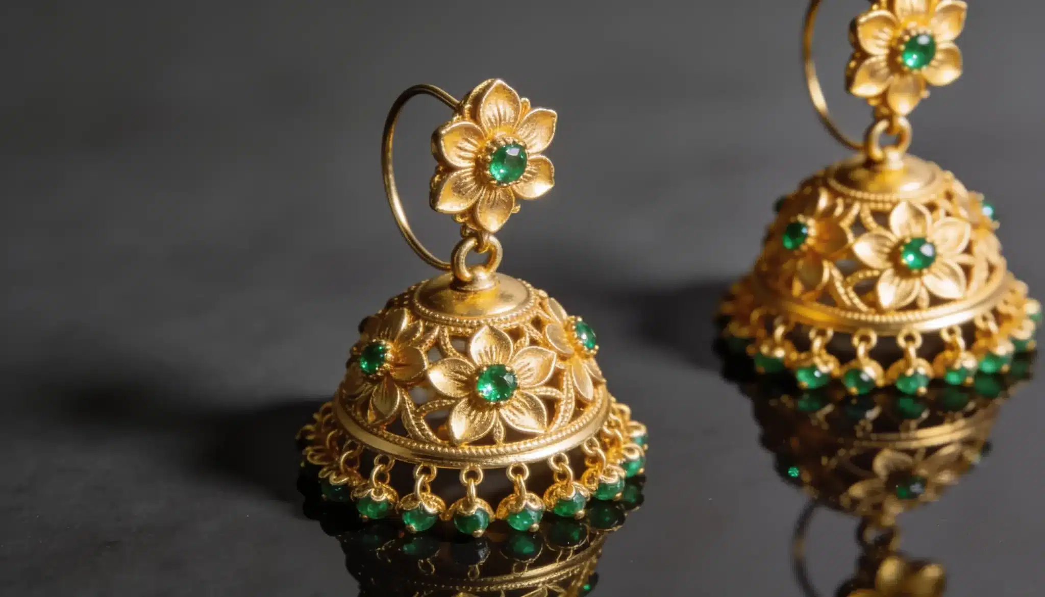 Gold jhumka earrings with green stone accents and floral detailing.