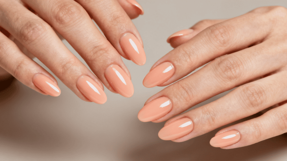 Hands showing almond nails in light peach shade with glossy finish, warm playful summer look.