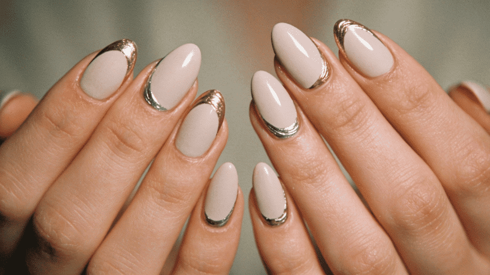 Hands showing almond nails with metallic gold and silver accents over nude base, modern chic look.