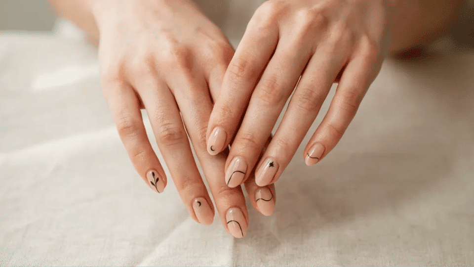 Hands showing almond nails with minimalist thin line art on nude base, elegant creative look.