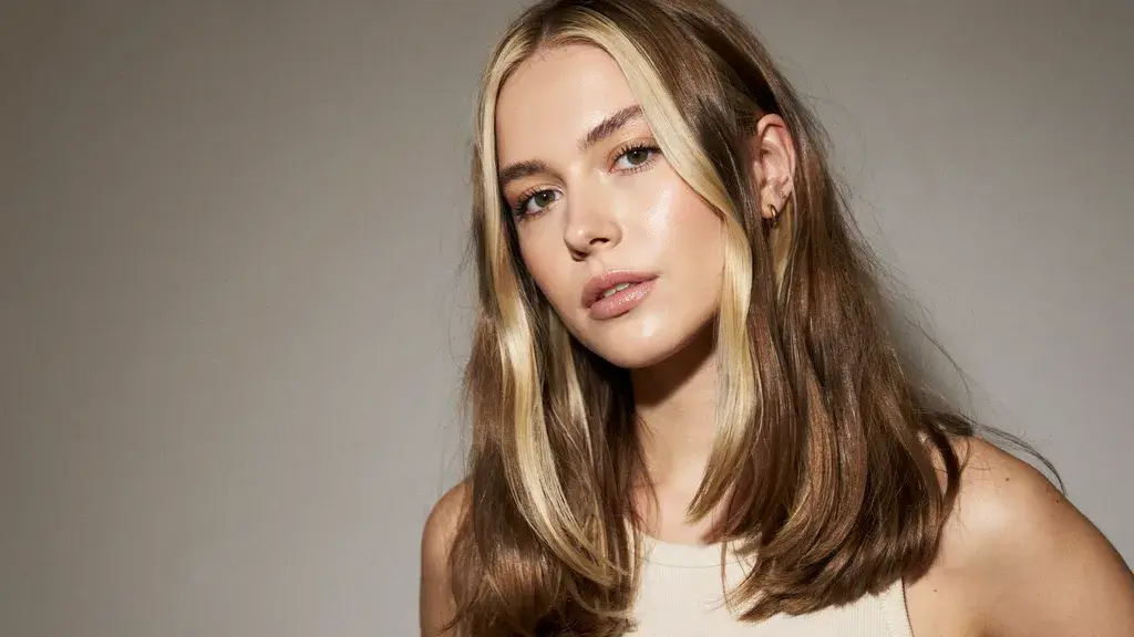 Brunette hair with bright blonde money piece highlights framing the face.