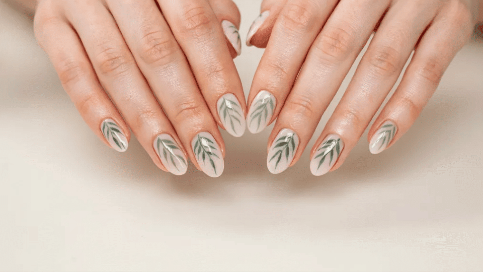 Almond nails with palm leaf accents on cream base, matte and glossy finish, tropical vacation-ready manicure.