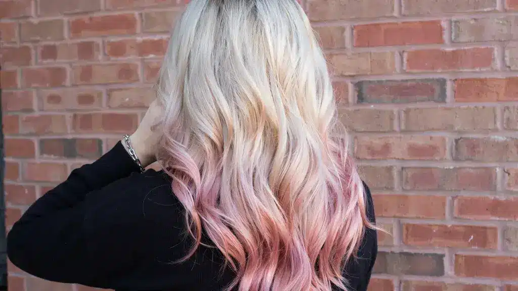 Back view of platinum blonde wavy hair with a subtle pastel pink peekaboo hair color technique at the ends.