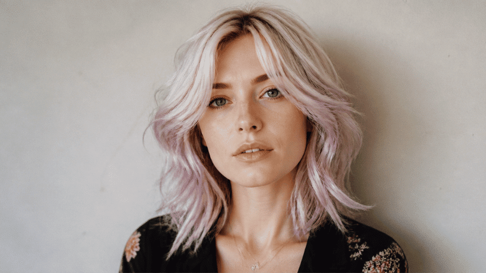 Woman with platinum blonde hair subtly tinted with lavender, styled in soft waves.