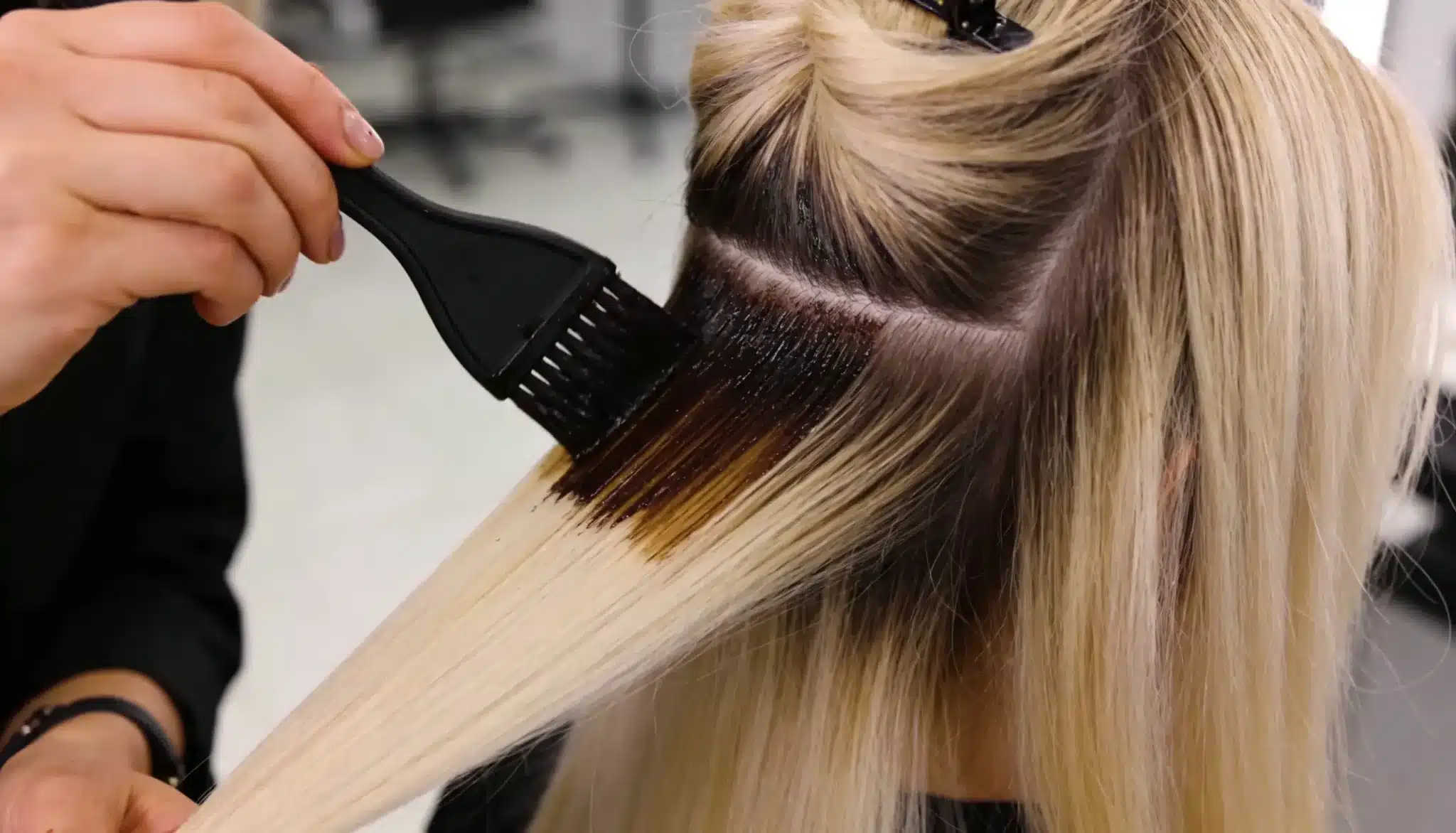 Stylist blending darker root color into blonde highlights using a root smudge technique.