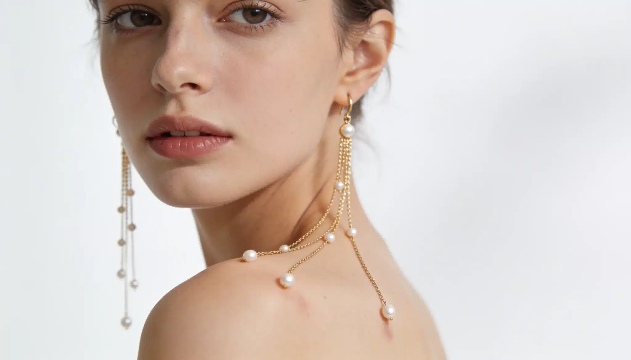 Woman wearing long pearl shoulder duster earrings with cascading chains.