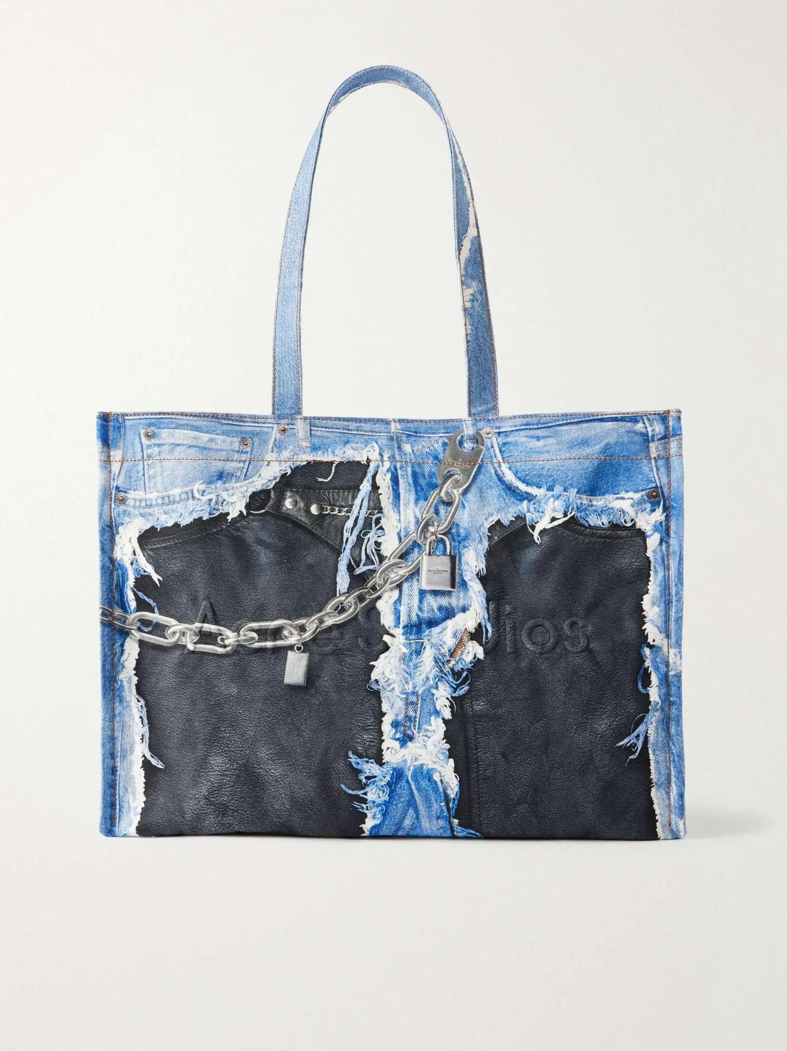 Blue denim tote bag with frayed patches and silver chain details against a neutral background