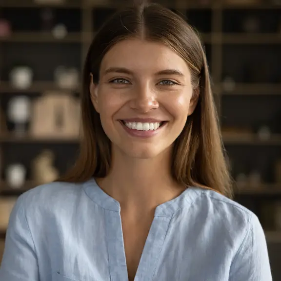 Smiling woman in light blue blouse with bookshelf background in soft natural light