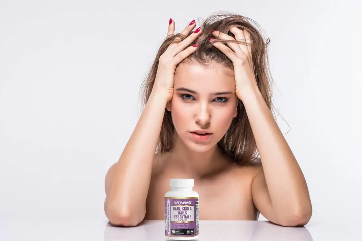 Woman touching her hair with vitamins bottle on white surface in bright studio