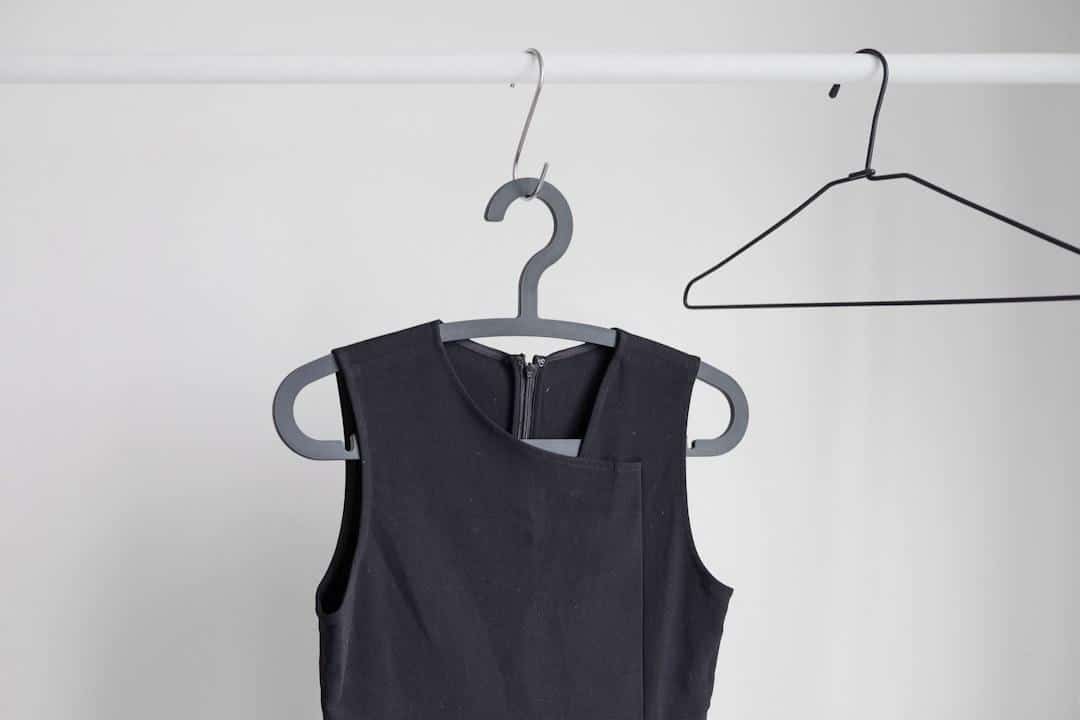 Elegant black party dress on a hanger against a plain wall