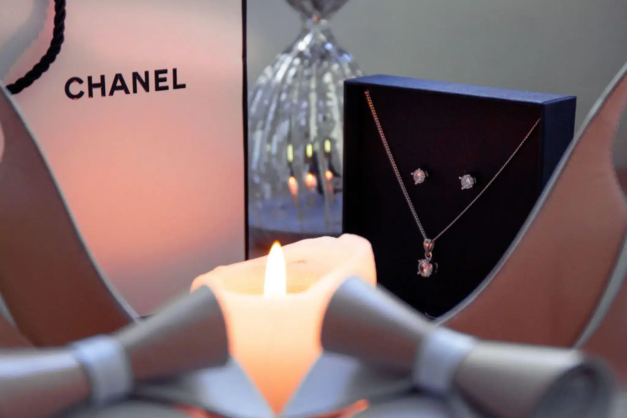 Jewelry set with necklace and earrings next to lit candle and Chanel gift bag