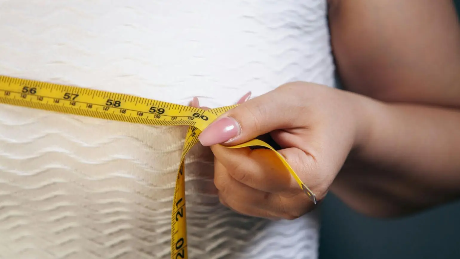 Hand holding yellow tape measure around person's waist in close-up shot