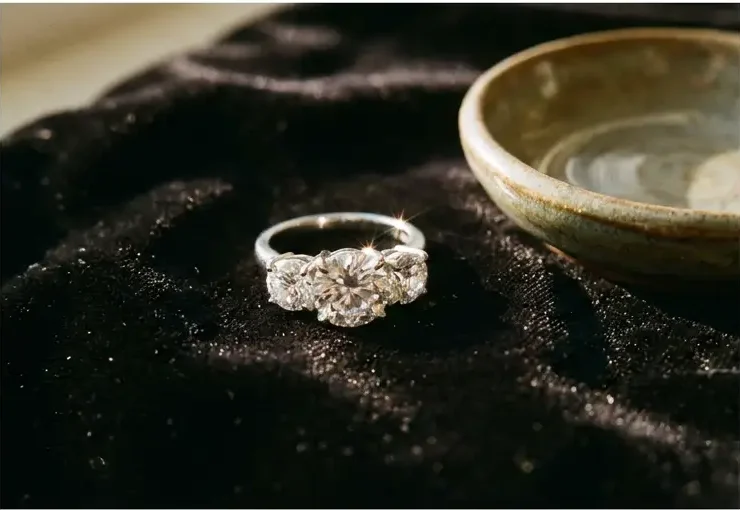 Diamond ring with multiple stones on black velvet beside a ceramic dish