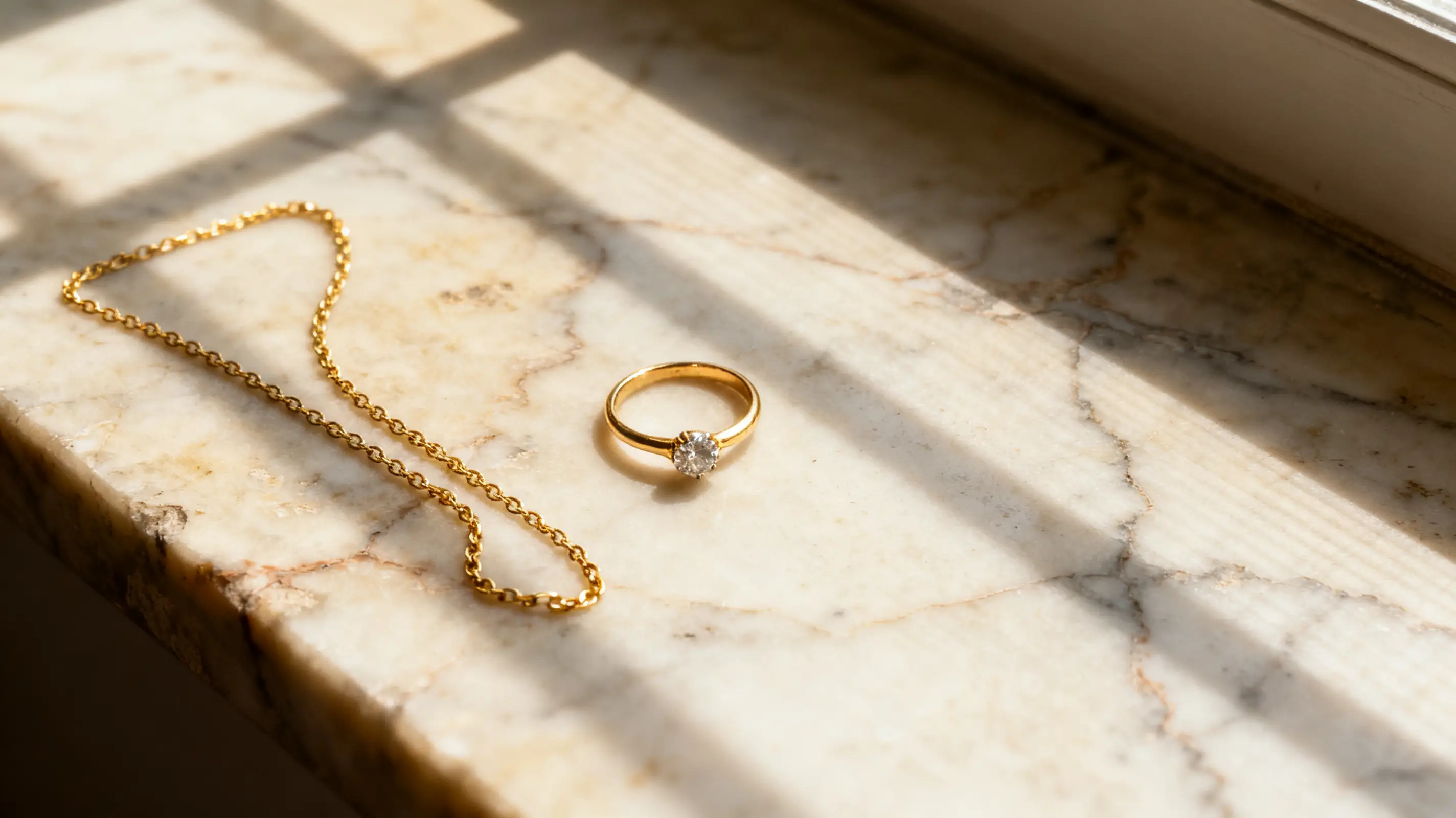 Gold chain and diamond ring on sunlit marble surface